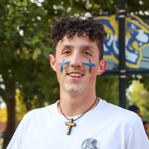 Student wearing face paint and a cross necklace on campus at a Christian College, reflecting faith, school spirit, and student community.