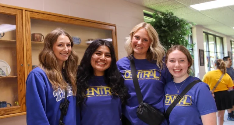 Group of smiling students wearing Central Christian College shirts indoors, representing campus visitors and community members who may benefit from local hotel discounts.